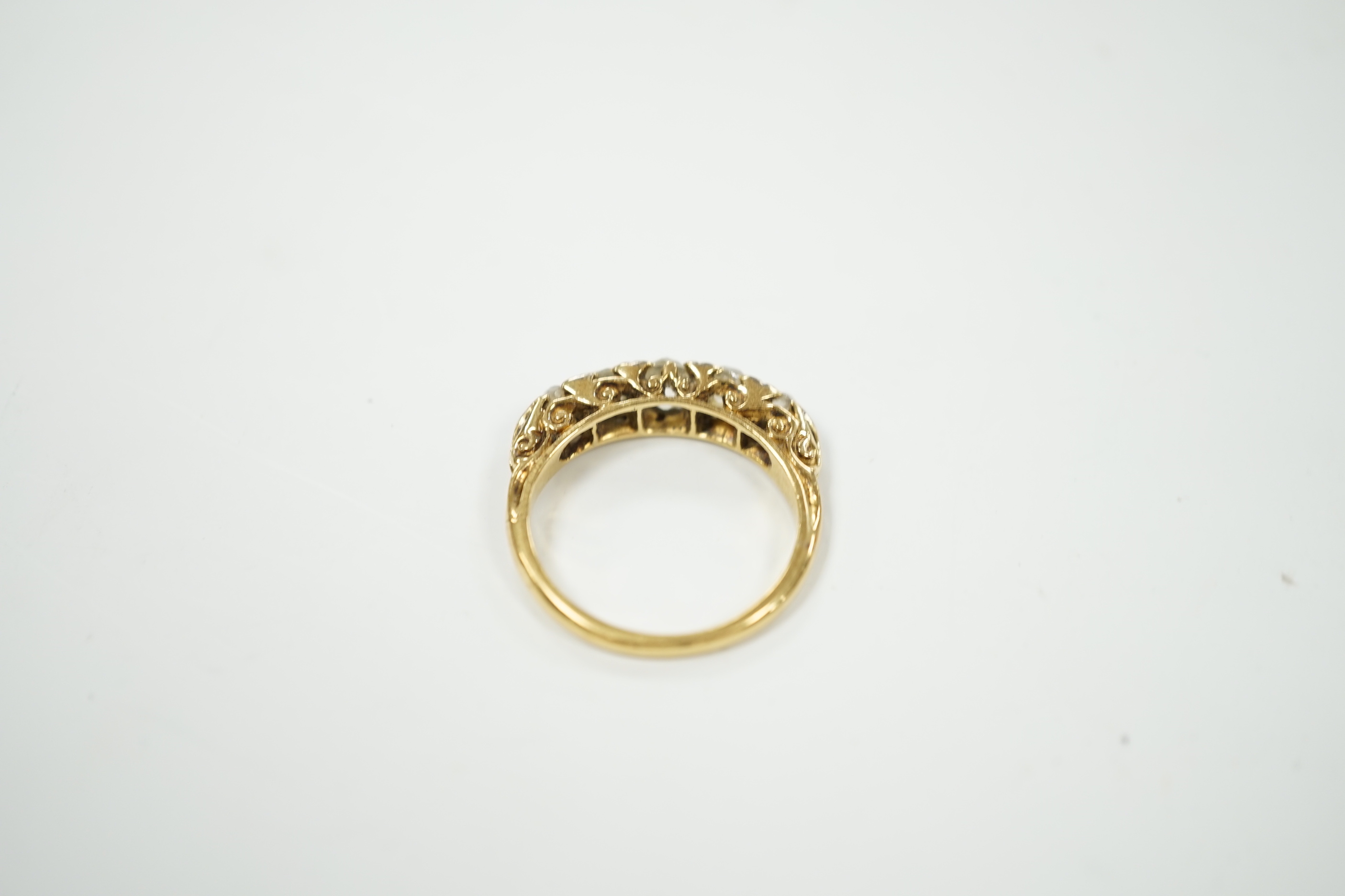 An early 20th century yellow metal and graduated five stone diamond set half hoop ring, with diamond chip spacers, size N/O, gross weight 4.7 grams.